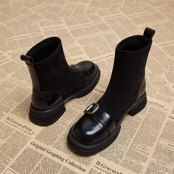 Black version of the suede boots with glossy black leather toe caps, brass-toned buckle straps and back pull tabs, seen from an angle.