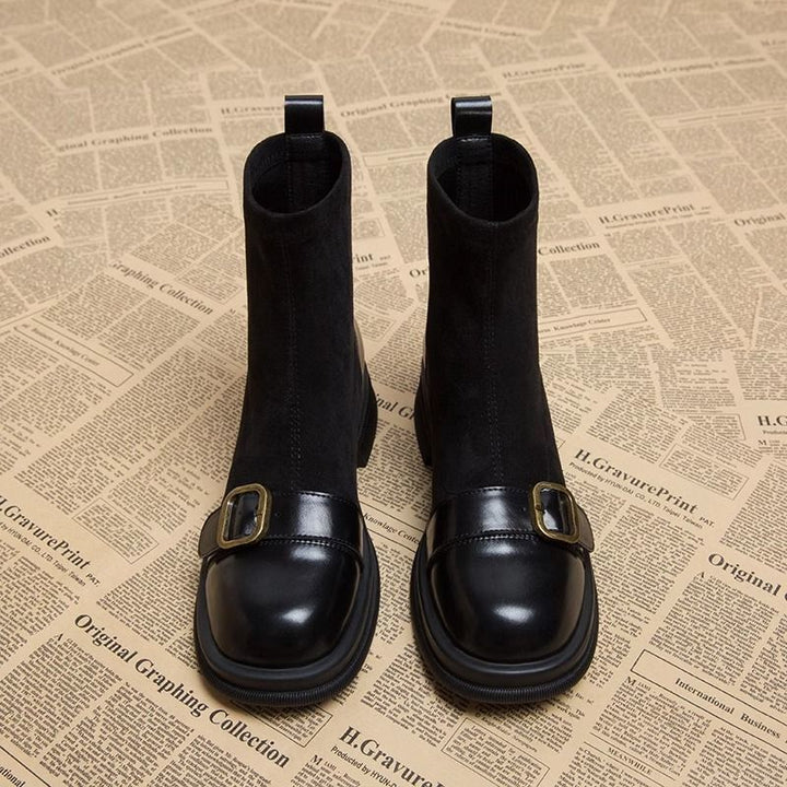 Front view of black suede boots with round leather toe caps, buckle straps and thick rubber soles side by side.
