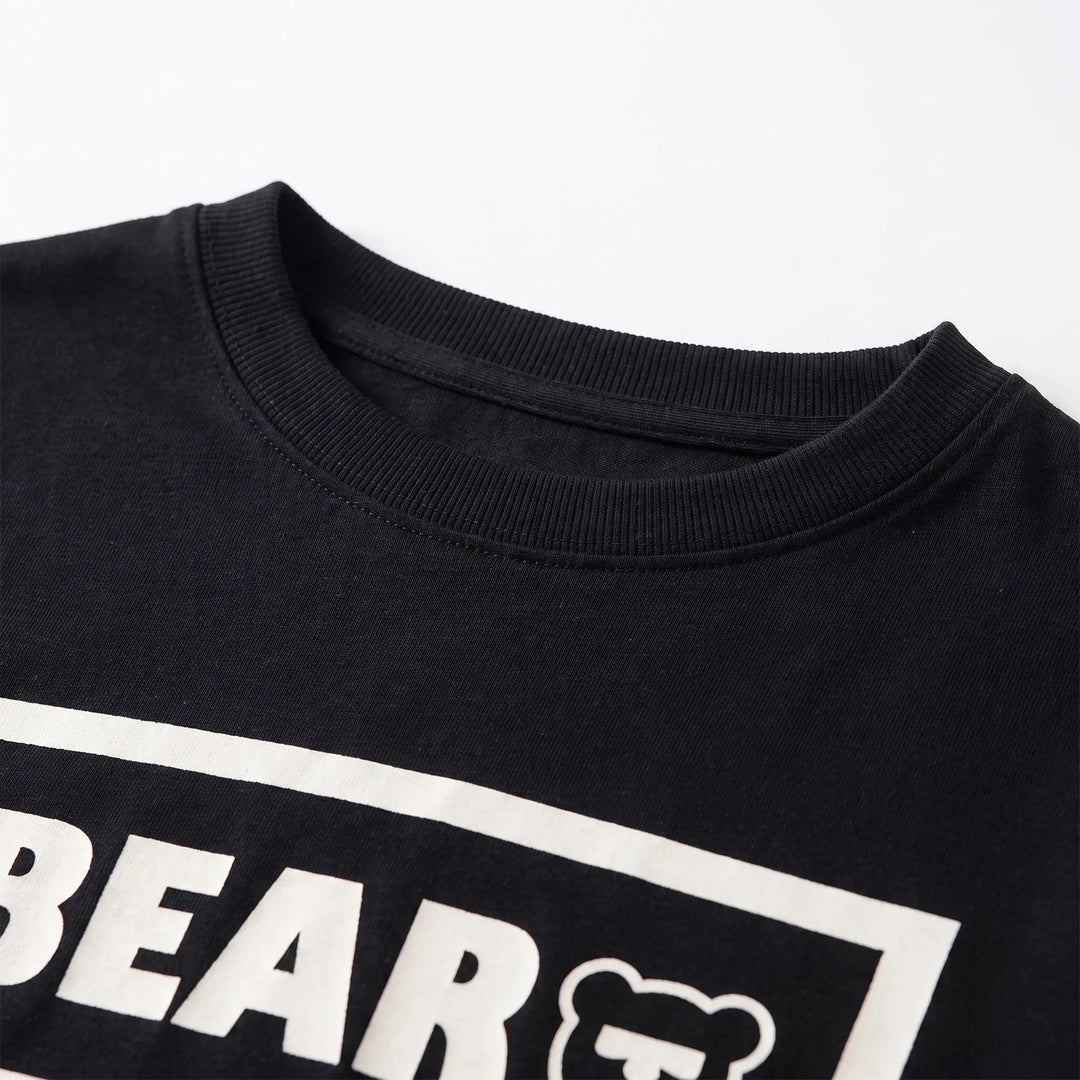 Close-up of the black crew neckline with ribbed collar and stitching, showing part of the white boxed print below. 4