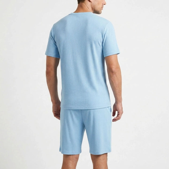 Back view of a man wearing the light blue ribbed pajama top and shorts, showing the plain back and vertical ribbing. 3