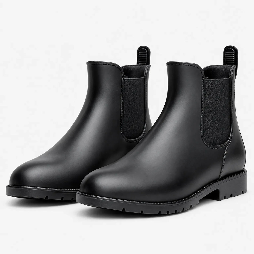 Pair of matte black Chelsea rain boots with elastic side panels, pull tabs and lugged soles on a plain white background. 2