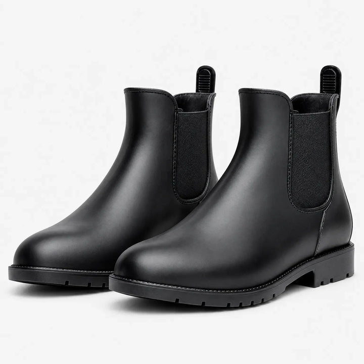 Pair of matte black Chelsea rain boots with elastic side panels, pull tabs and lugged soles on a plain white background. 2