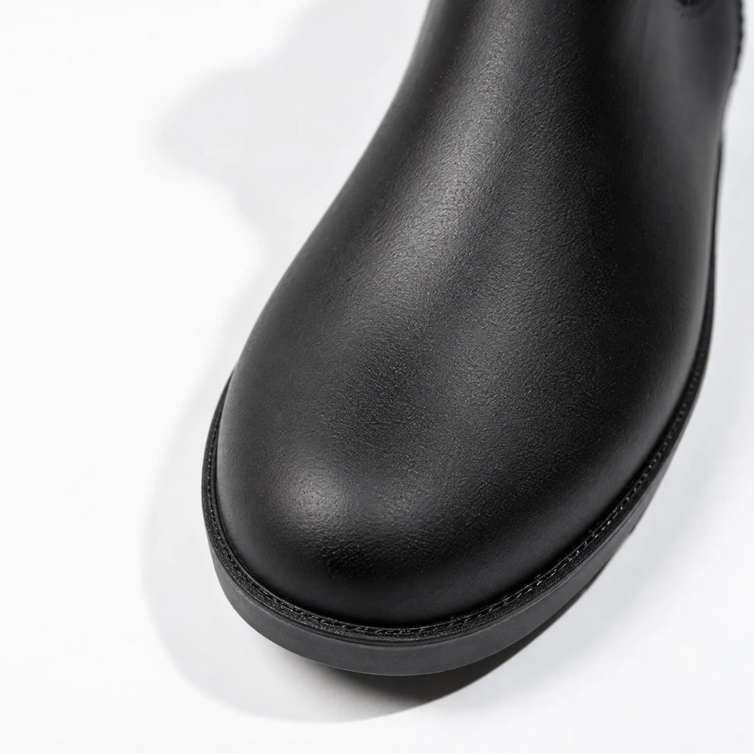 Close-up of the rounded toe of a black rain boot, showing the textured matte finish and stitched edge above the sole. 6