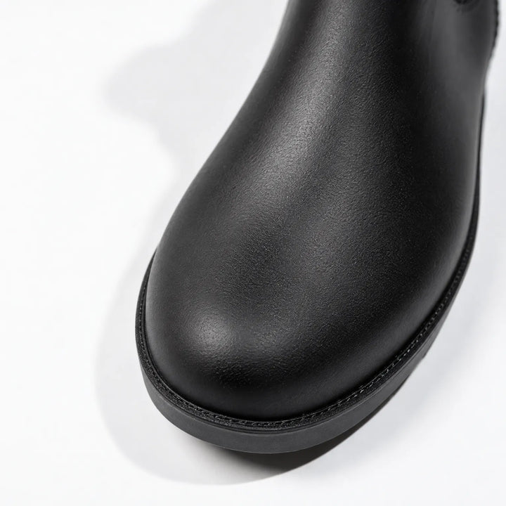 Close-up of the rounded toe of a black rain boot, showing the textured matte finish and stitched edge above the sole. 6