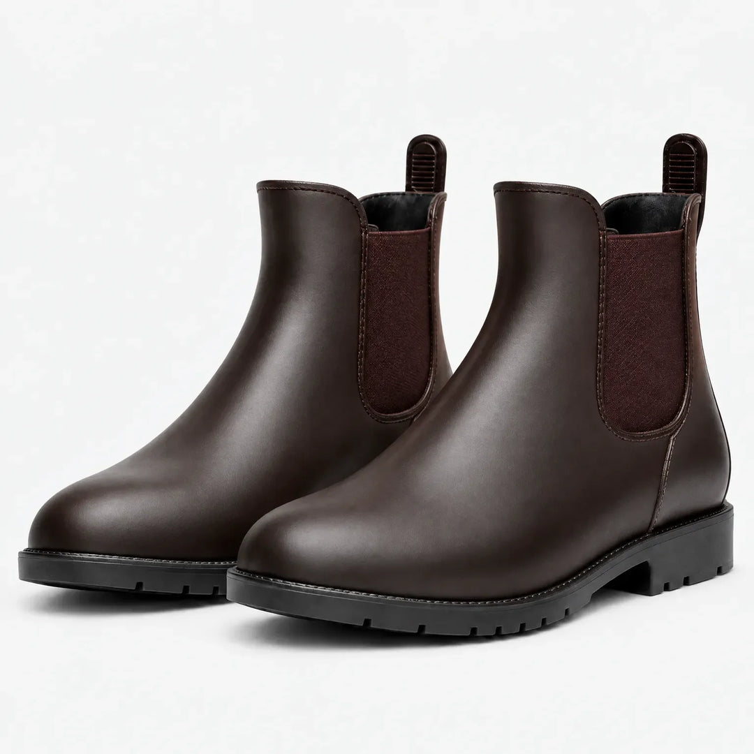 Pair of dark brown Chelsea rain boots with maroon elastic side panels, pull tabs and black lugged soles on a white background. 7