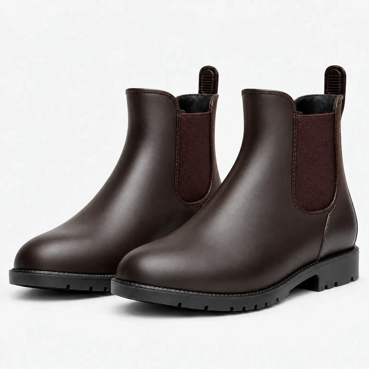 Pair of dark brown Chelsea rain boots with maroon elastic side panels, pull tabs and black lugged soles on a white background. 7
