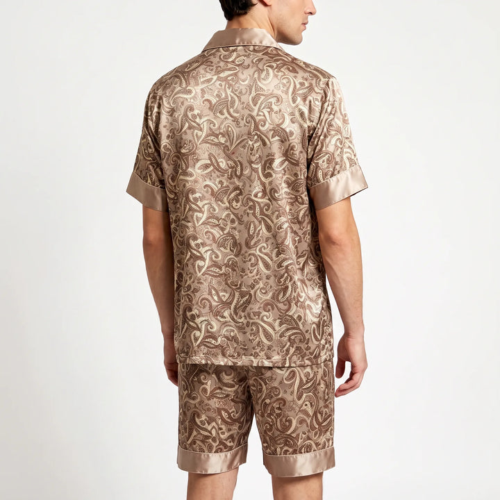 Back view of a model wearing the tan paisley satin pajama shirt and shorts with wide contrast cuffs. 2