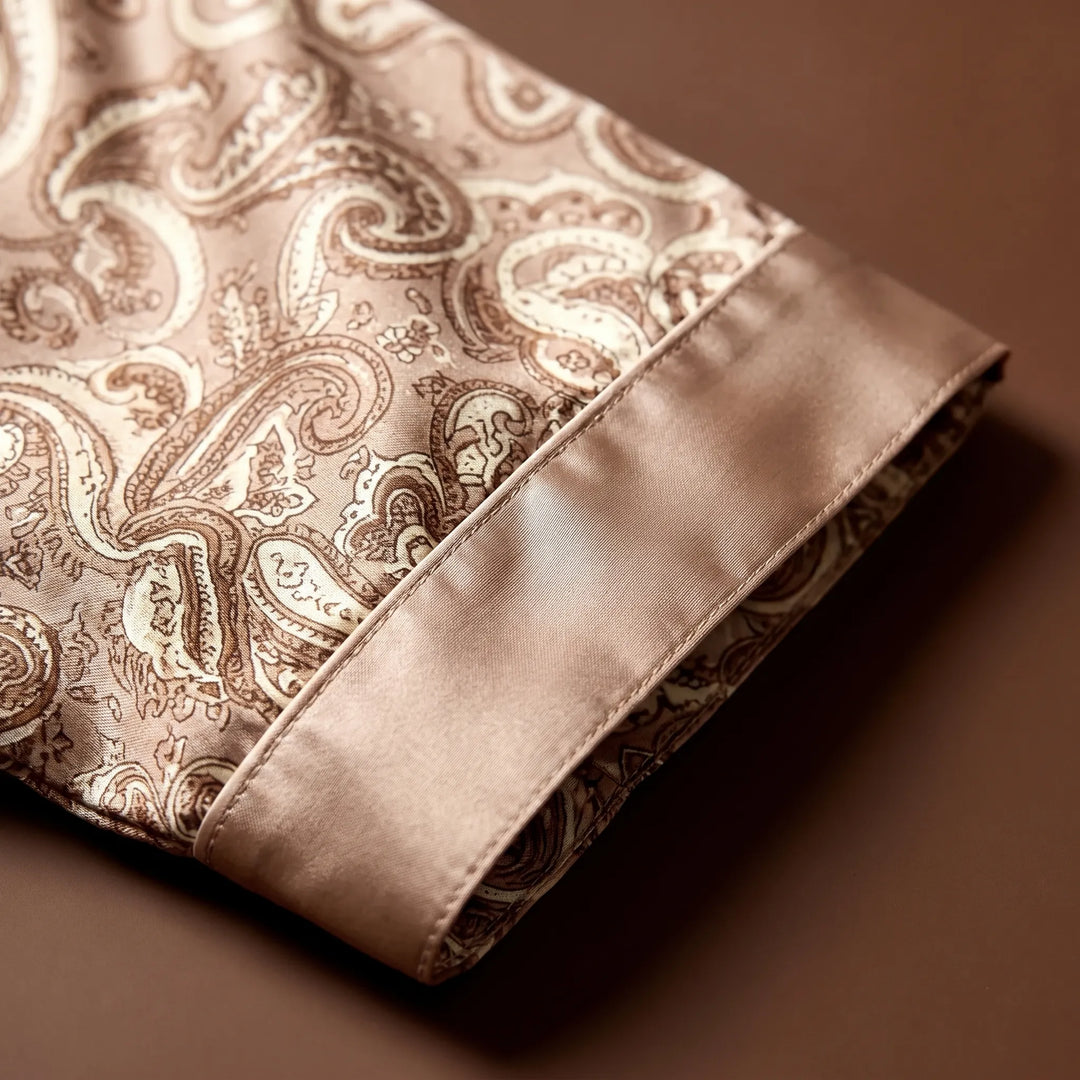 Close-up of a sleeve cuff with smooth satin contrast trim, piping and stitching beside the tan paisley print. 4