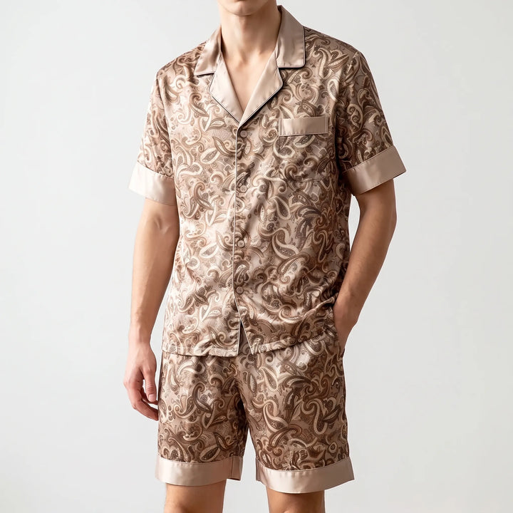 Model standing with one hand in a shorts pocket, wearing the tan paisley satin pajama set on a light background. 6