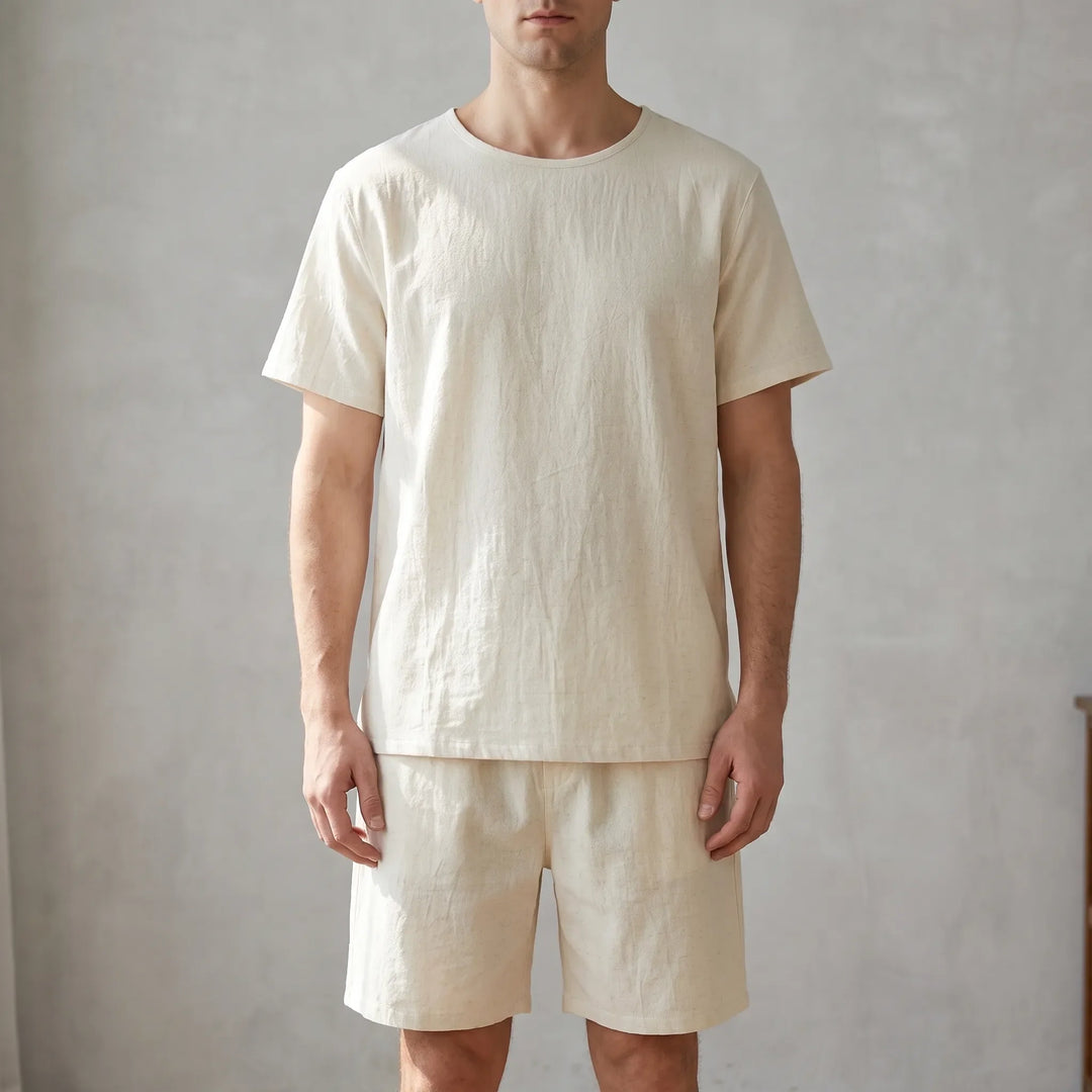 Man standing against a textured gray wall wearing the cream crew-neck tee and matching shorts, shown from the front. 1