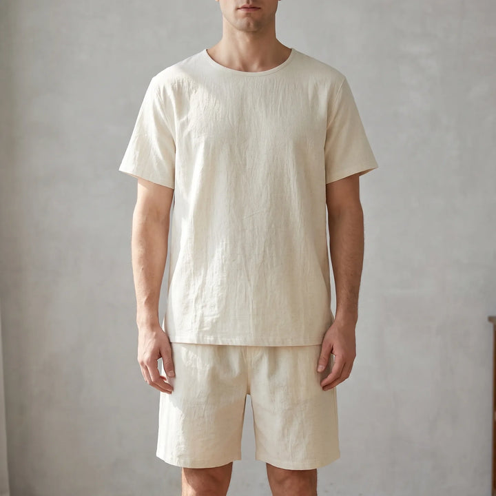 Man standing against a textured gray wall wearing the cream crew-neck tee and matching shorts, shown from the front. 1