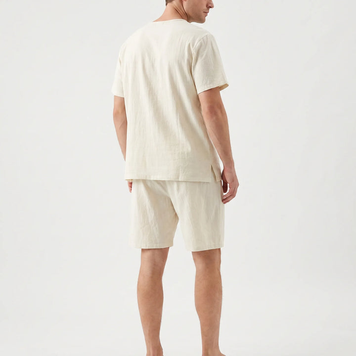 Back view of the cream pajama set on a model, showing the small side slit at the tee's hem and the shorts. 3