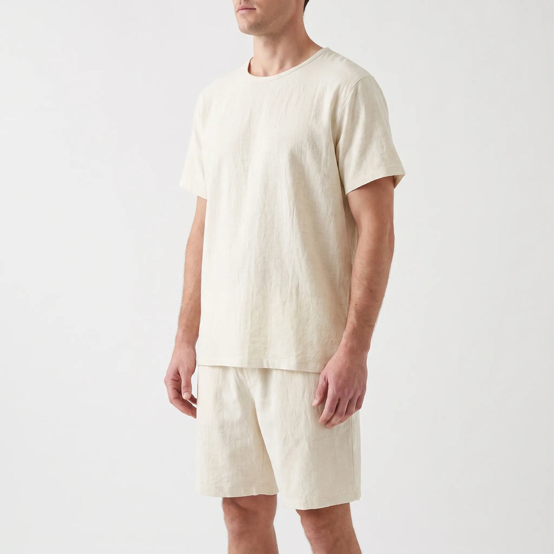 Three-quarter angle of a model in the cream short-sleeve tee and drawstring-style shorts, arms relaxed at his sides. 4