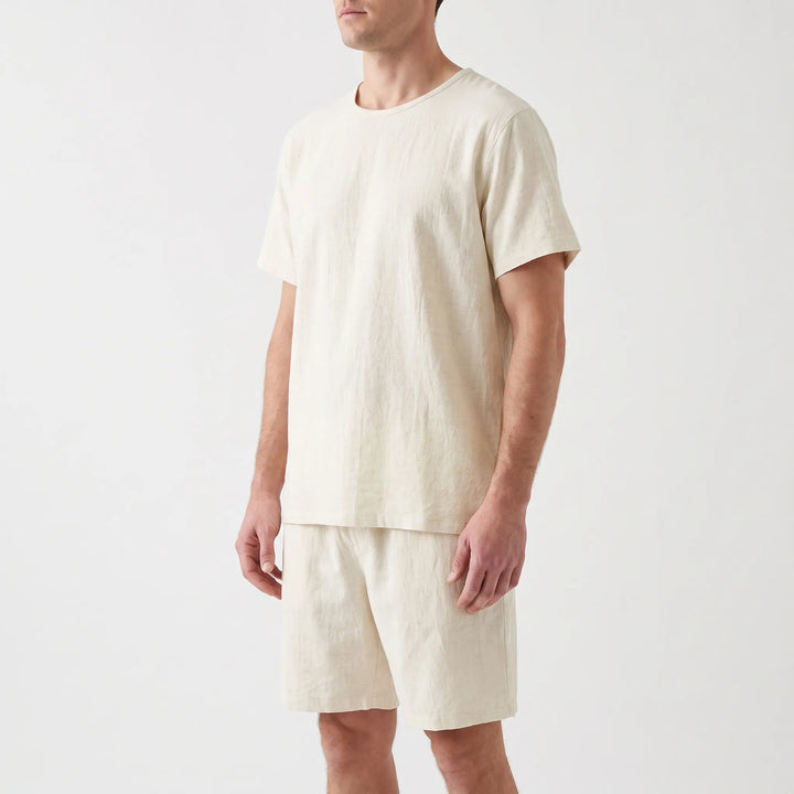 Three-quarter angle of a model in the cream short-sleeve tee and drawstring-style shorts, arms relaxed at his sides. 4