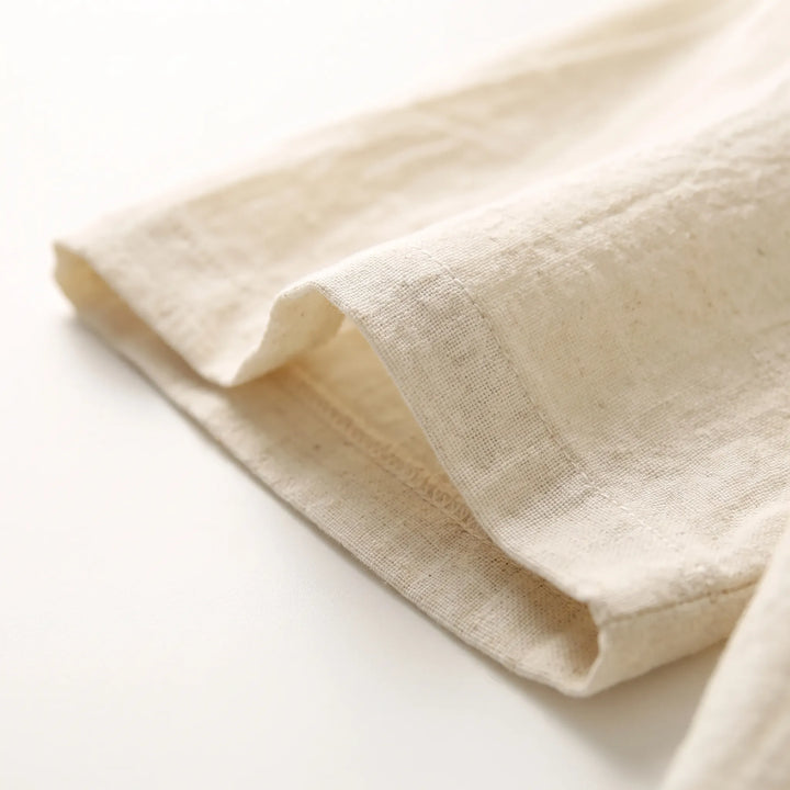 Close-up of a stitched hem of cream woven fabric, showing the fine texture and seam detail. 5