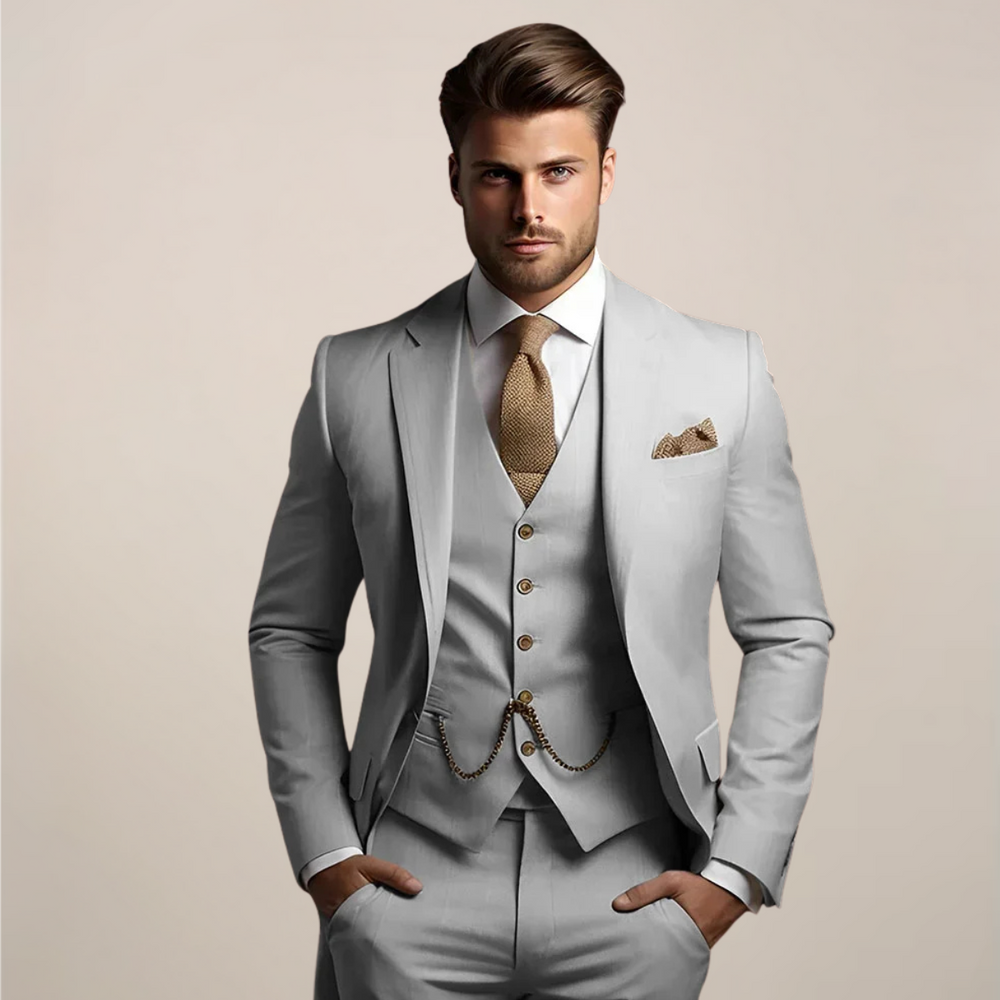 Men's three-piece suit in light gray with a white shirt, tan knit tie and gold vest chain.