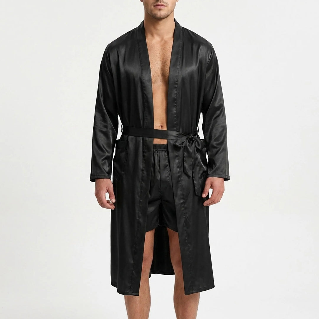 Front view on a white background of a model wearing the black satin robe open and belted, with matching satin boxer shorts. 2