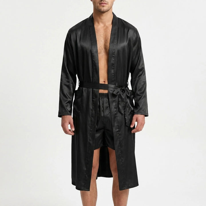 Front view on a white background of a model wearing the black satin robe open and belted, with matching satin boxer shorts. 2