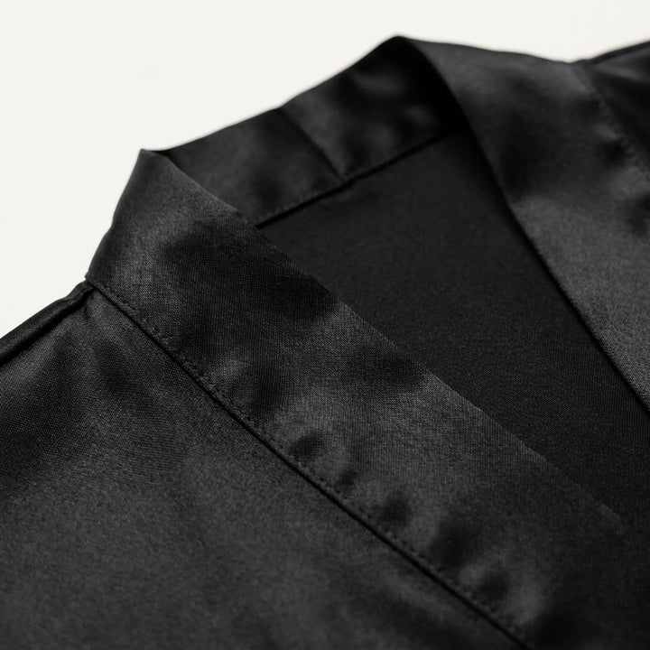 Close-up of the black satin robe's shawl collar and stitched edge, showing the glossy fabric texture on a white background. 5