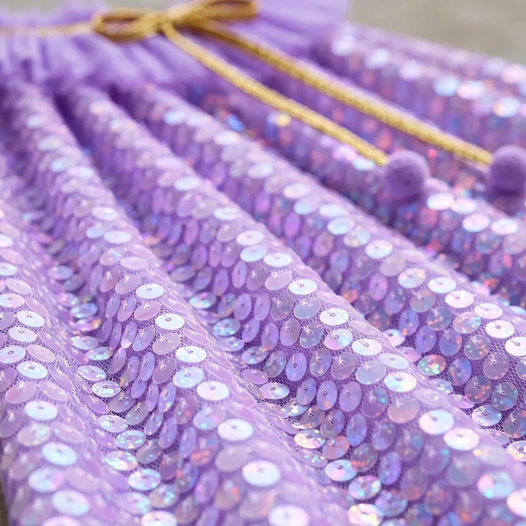 Close-up of the iridescent lavender sequins on the cape, with gold cord and purple pom-poms 3