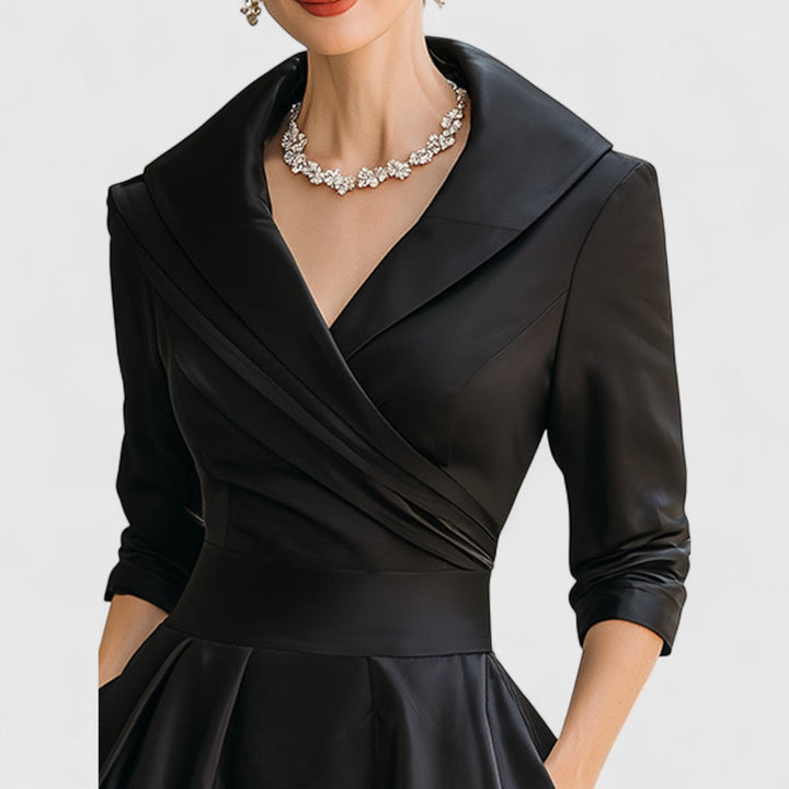 Close-up of the black dress bodice with a wide shawl collar, wrap pleats and rolled three-quarter sleeves.