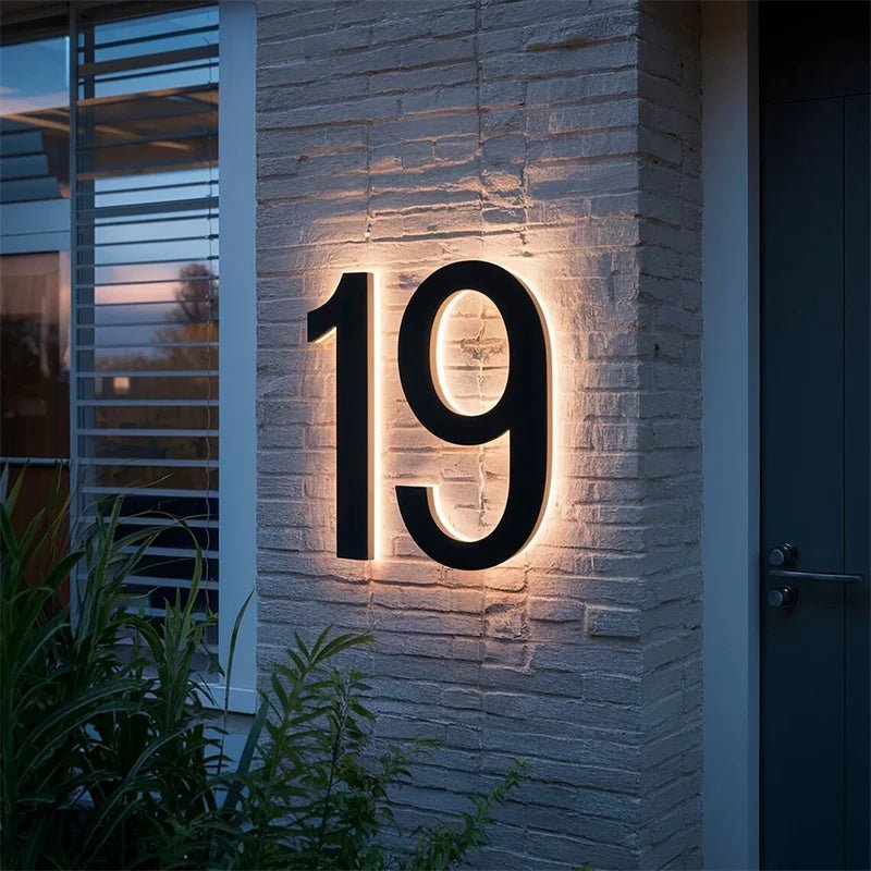 Large black two-digit house number with warm backlight on a white-painted brick wall.