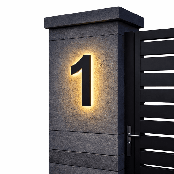 Black backlit house number 1 with a warm glow on a dark stone gate pillar beside a black metal gate.
