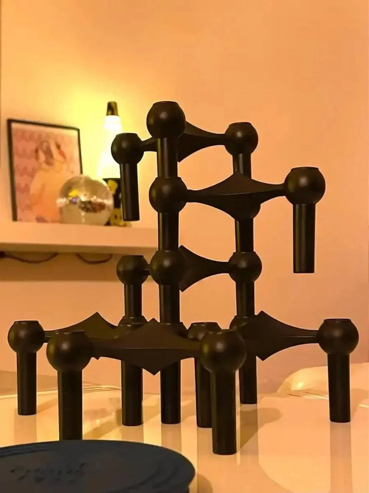 Black modular candle holder stacked on a glossy white surface with a softly lit shelf in the background.