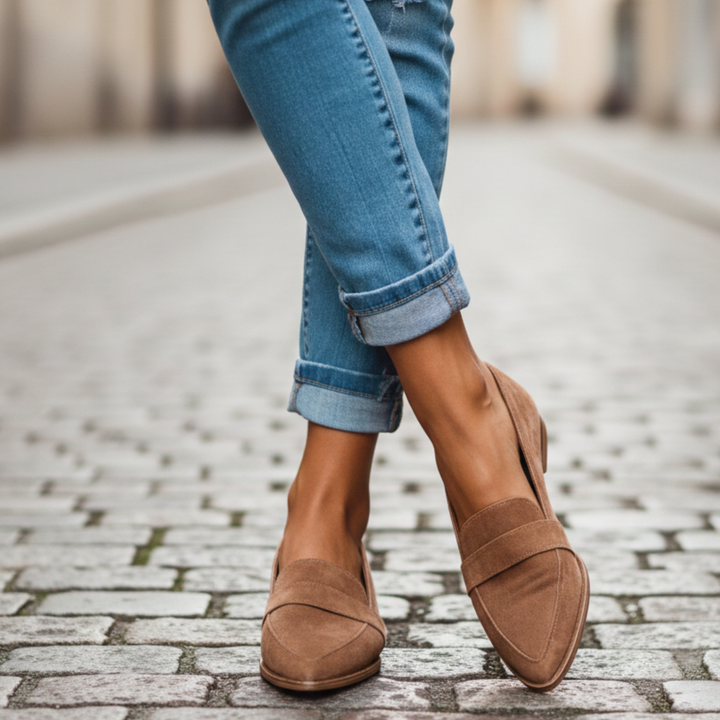 Tan suede pointed-toe loafers with a strap across the vamp, worn with cuffed jeans on a cobblestone street. 5