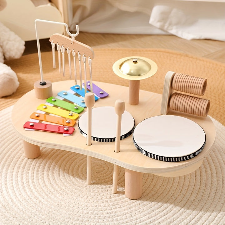 Wooden Montessori music table with rainbow xylophone, chimes, brass cymbal, two drums, and wooden mallets on a woven rug.