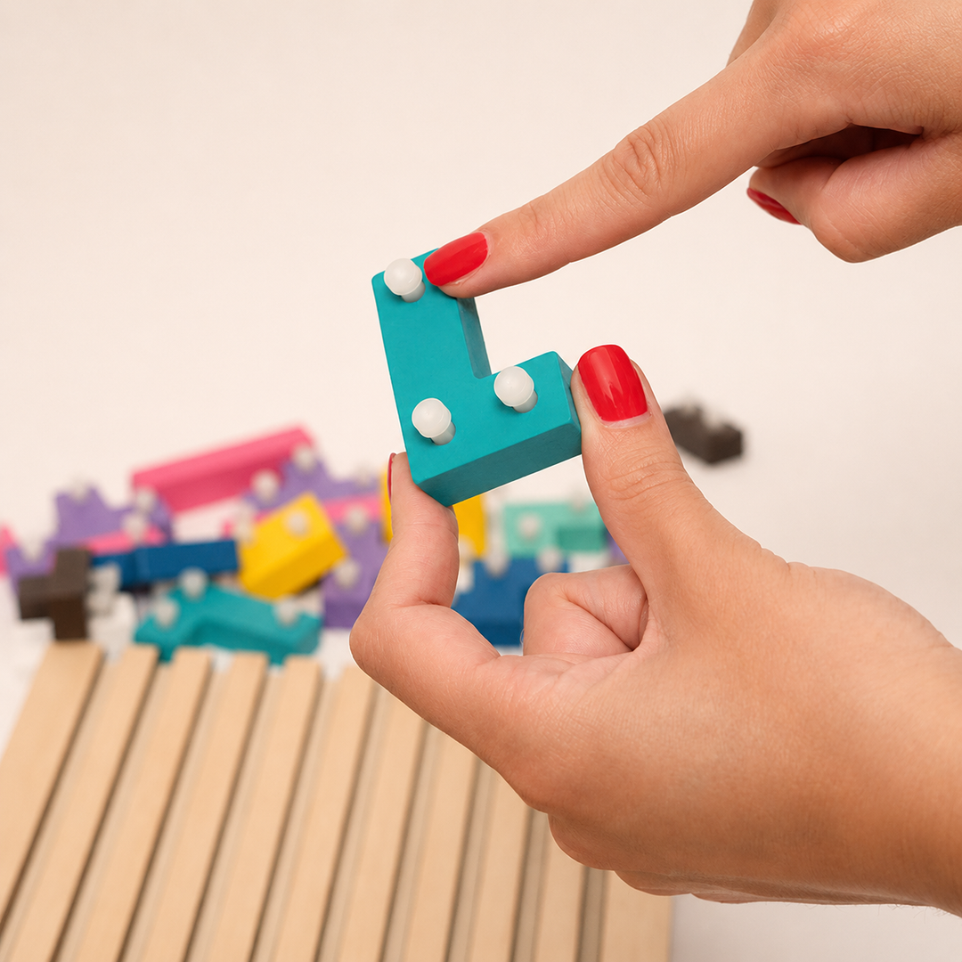 Fingers hold a teal L-shaped block that has three small white pegs on its back, with the slotted board blurred below. 15