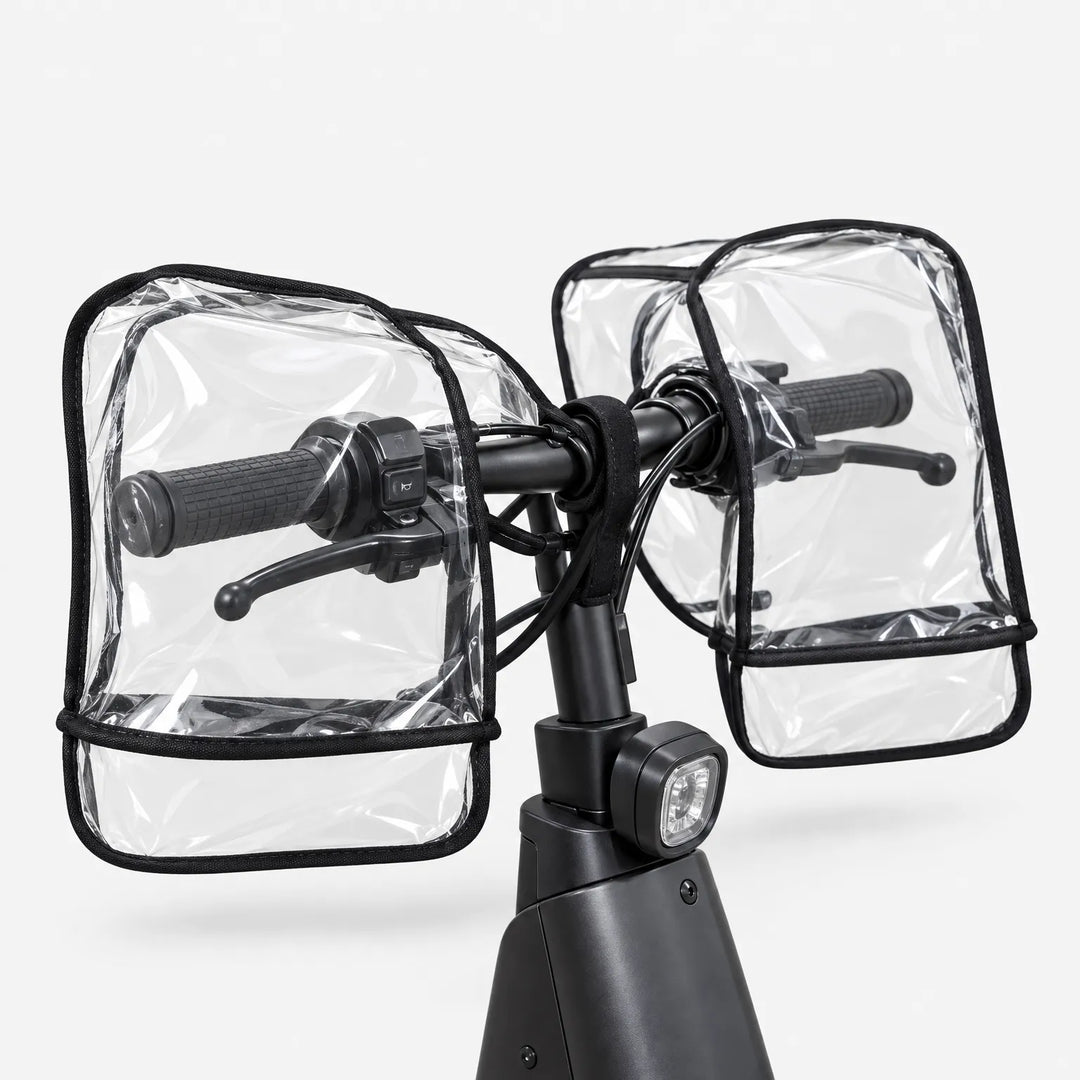 Rear angled view of clear handlebar muffs covering the grips and brake levers on a black scooter, against a plain background. 4