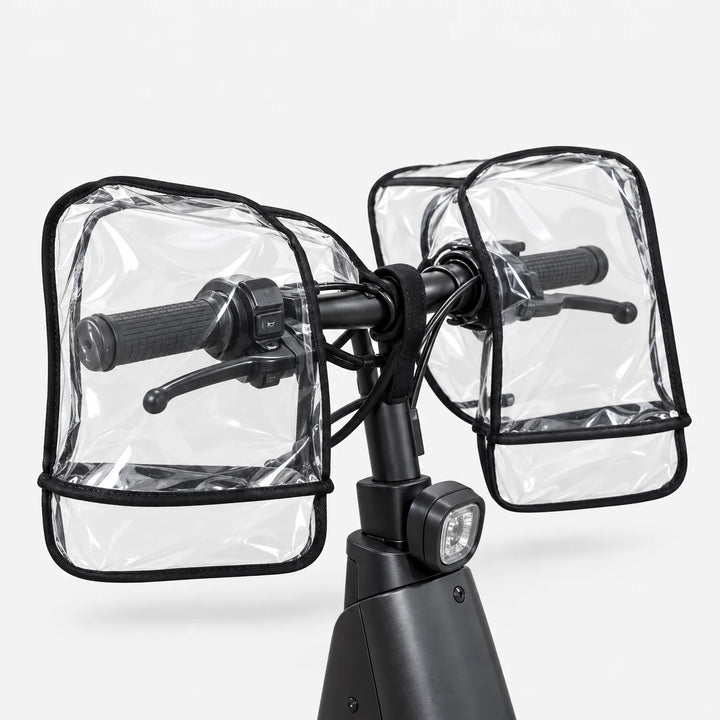 Rear angled view of clear handlebar muffs covering the grips and brake levers on a black scooter, against a plain background. 4