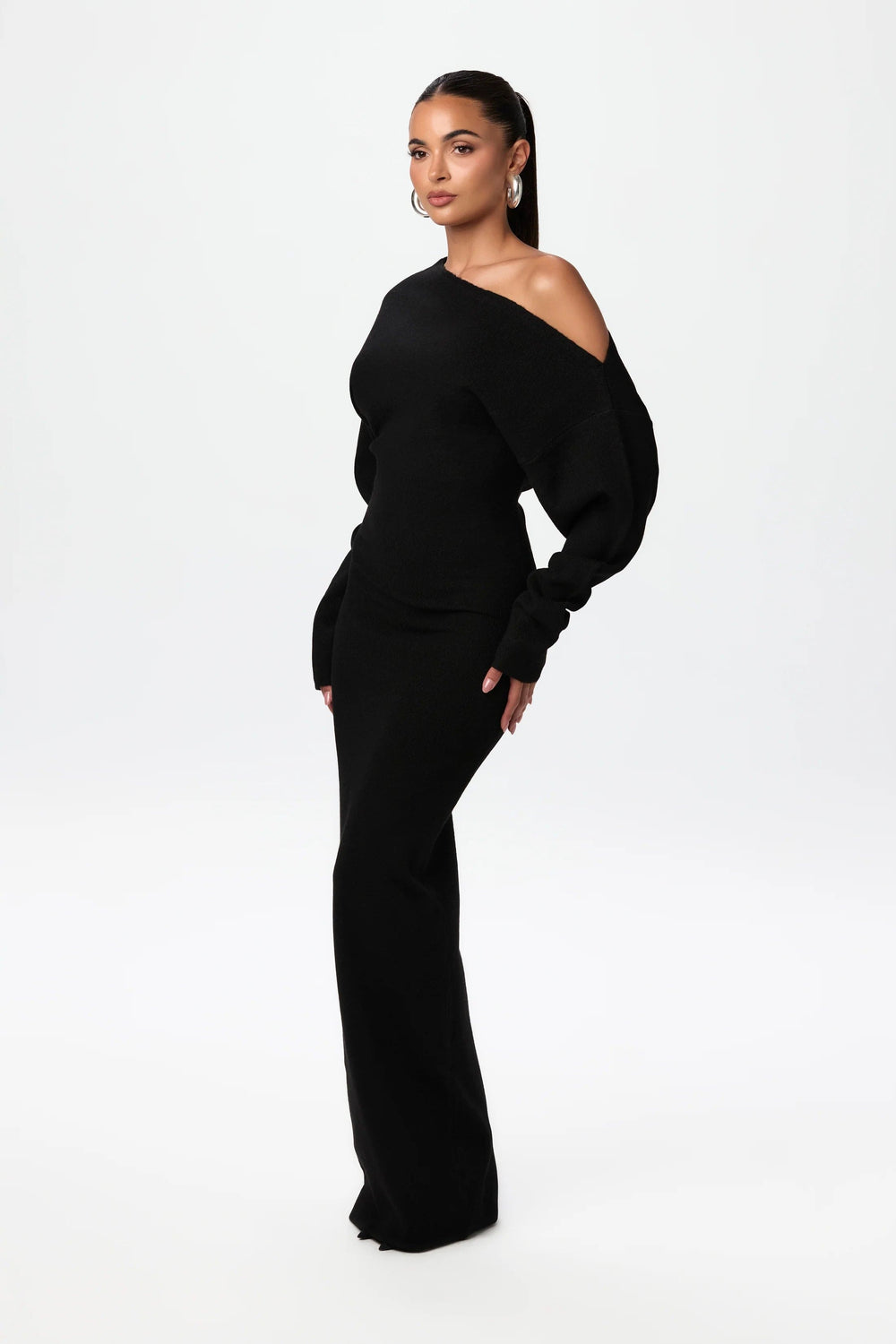 Three-quarter side view of the beige knit maxi dress, showing the asymmetric neckline and fitted skirt.