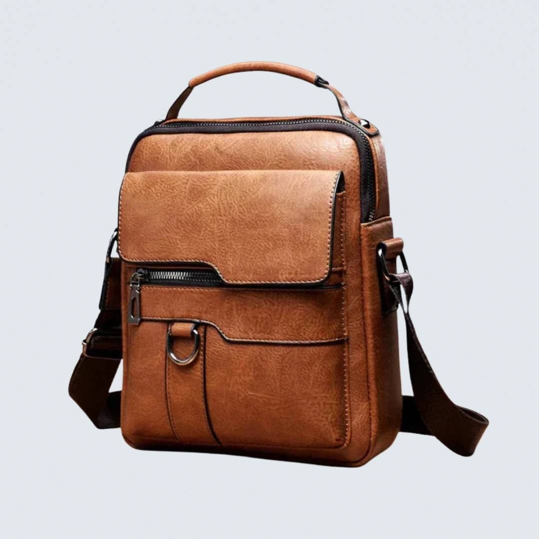 Brown leather shoulder bag with top handle, flap pocket and zipper, shown at a three-quarter angle.
