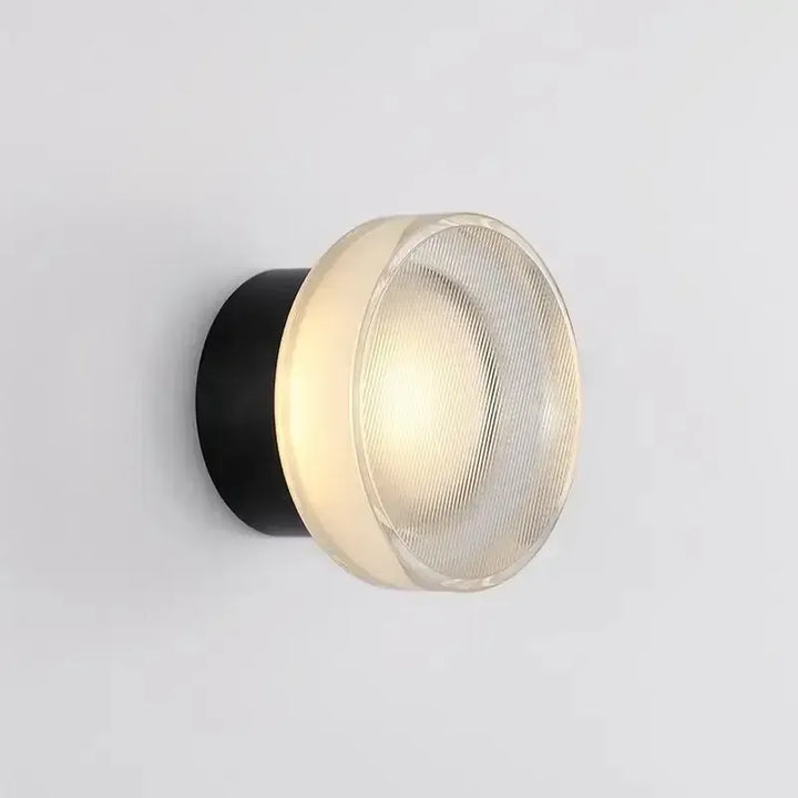 Round wall lamp with ribbed glass front and black backplate, lit with soft warm light.