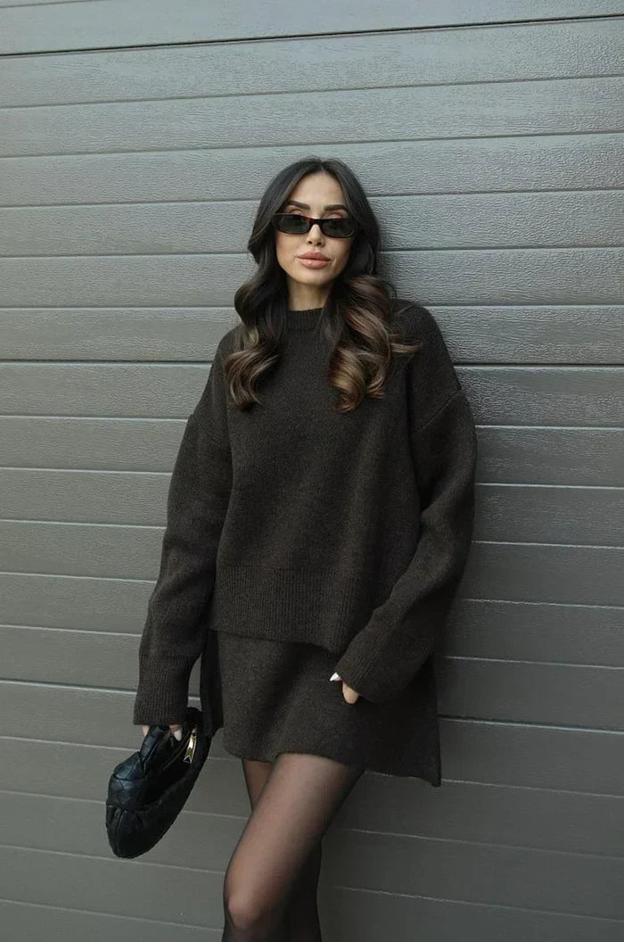 Dark brown knit sweater and skirt set, model leaning on a gray wall with a black woven bag 13