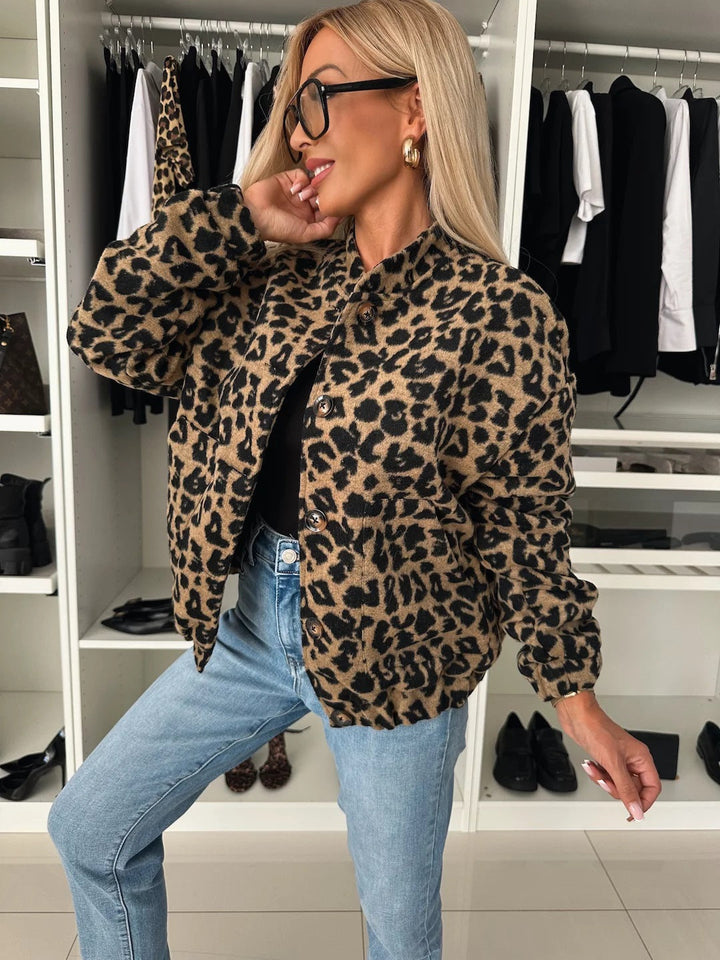 Woman in a leopard print button-front jacket with a stand collar, black top and light-wash jeans, hand raised to her face in a closet. 1