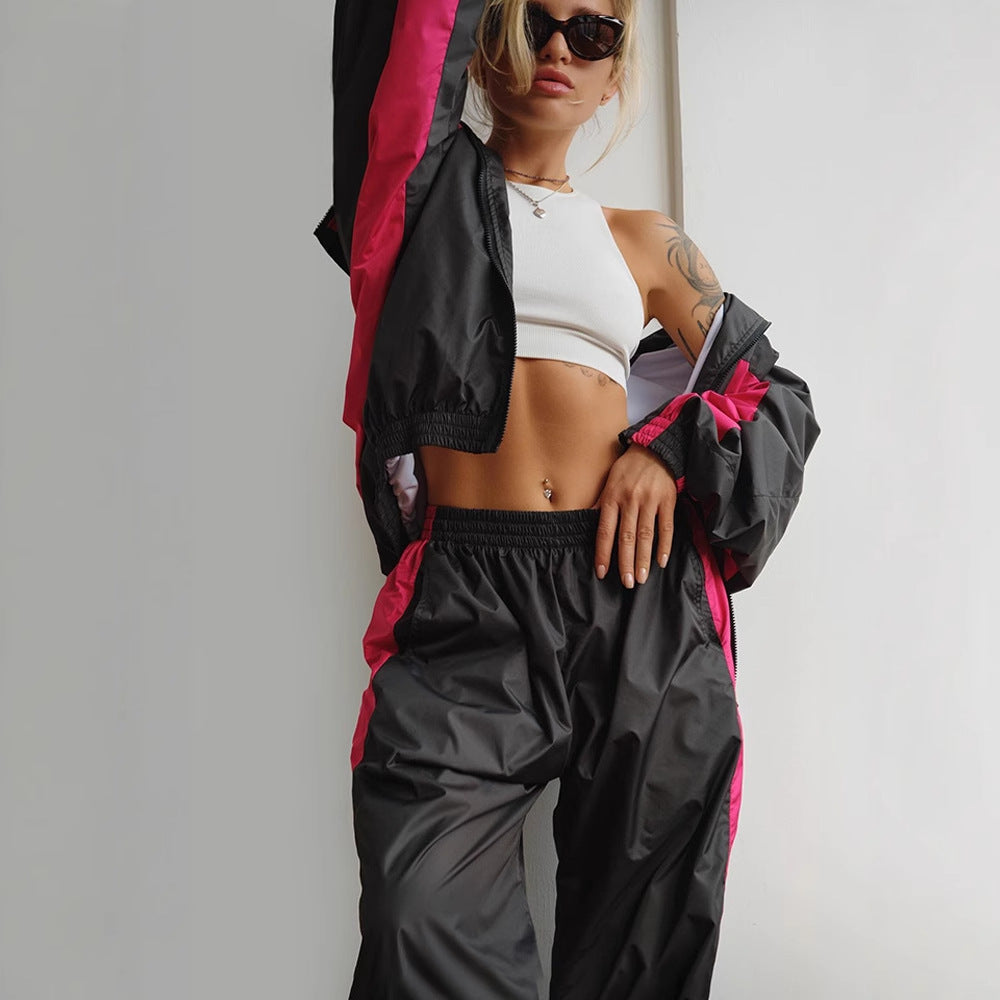 Women's windbreaker tracksuit set in black and hot pink, another view with the jacket worn off the shoulders.