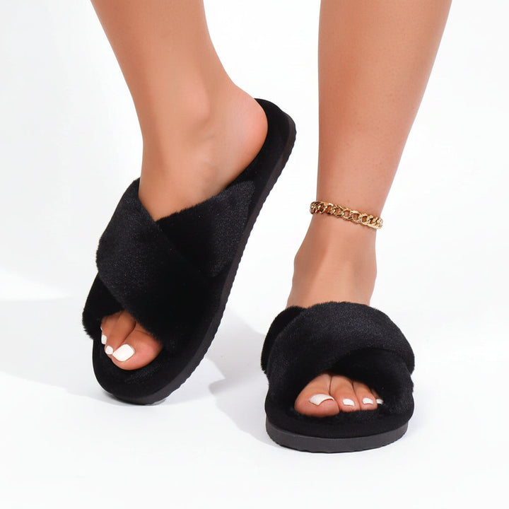 Model's feet in black fuzzy crossband slippers, one foot lifted, with a gold chain anklet 3