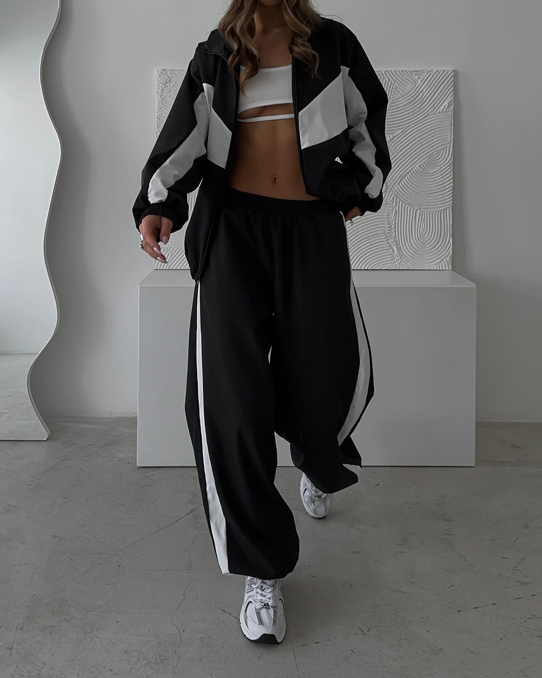 Model walking in the black set with white chevron panels on the cropped jacket and white side stripes on the wide-leg pants, with white sneakers. 21
