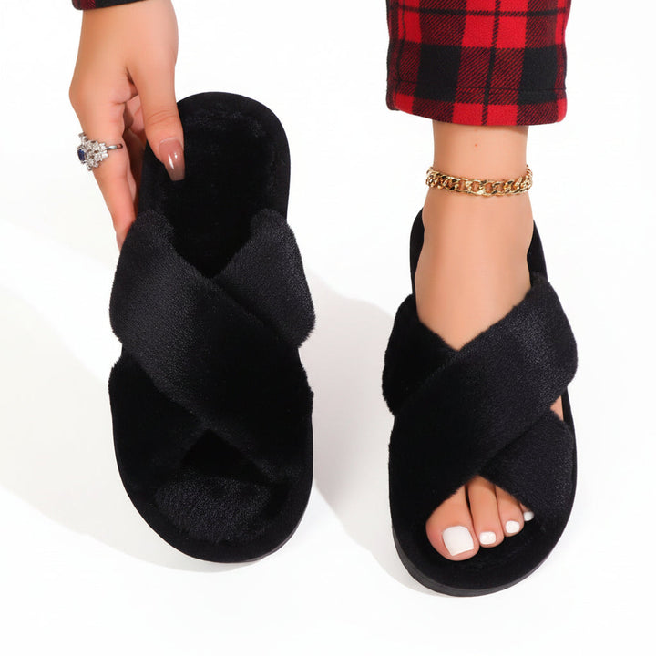 Black plush crossband slippers, one worn with red plaid pants and one held up 9