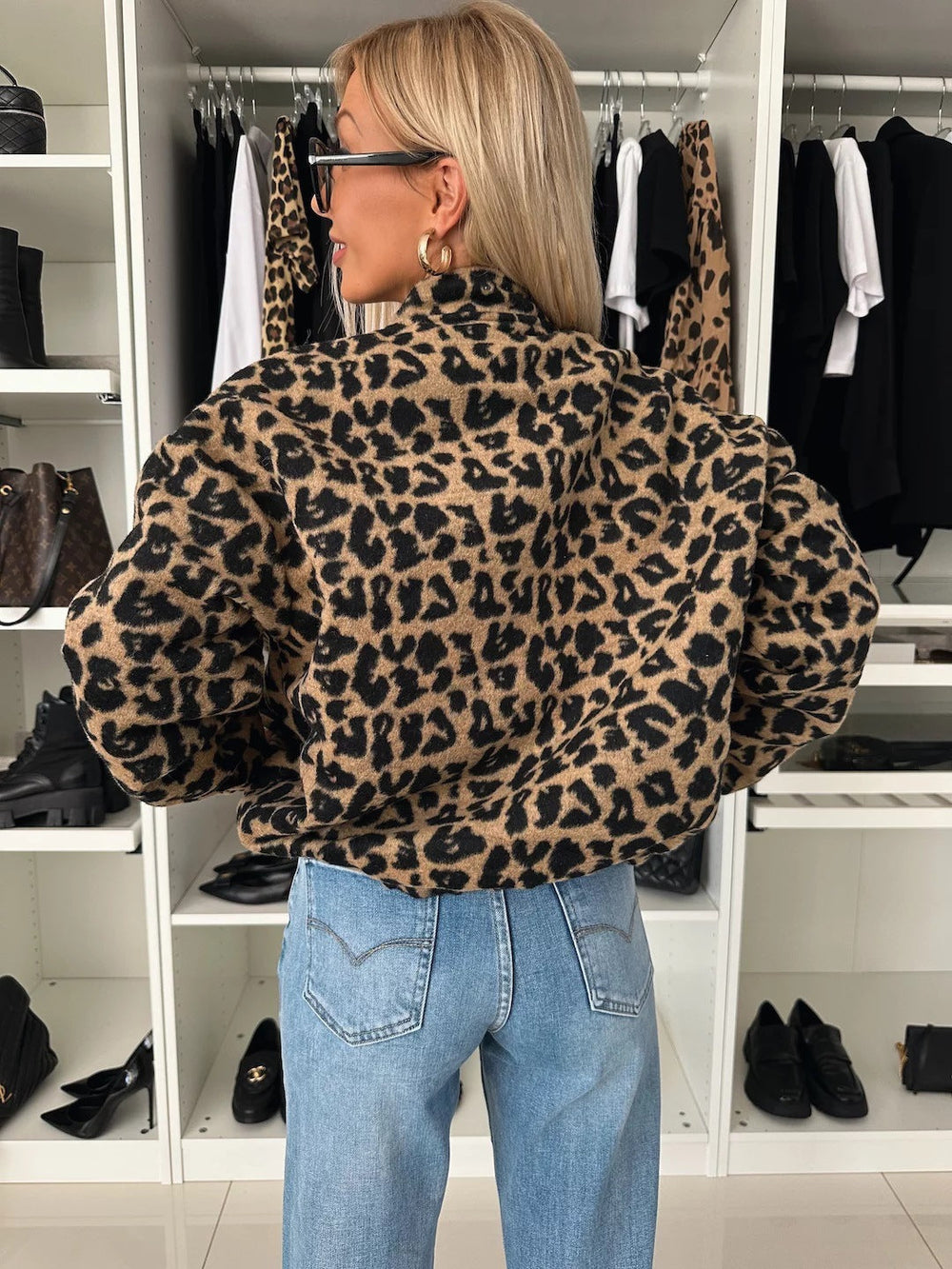 Back view of the leopard print jacket on a model, showing the stand collar, full sleeves and gathered hem over light-wash jeans. 2