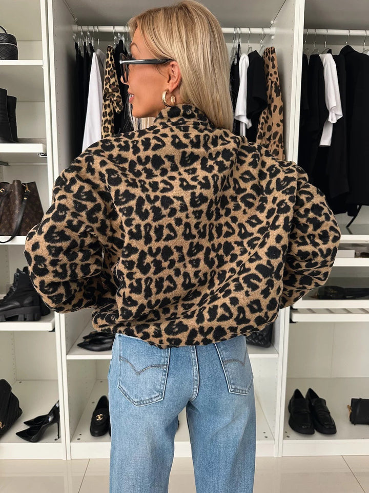 Back view of the leopard print jacket on a model, showing the stand collar, full sleeves and gathered hem over light-wash jeans. 2