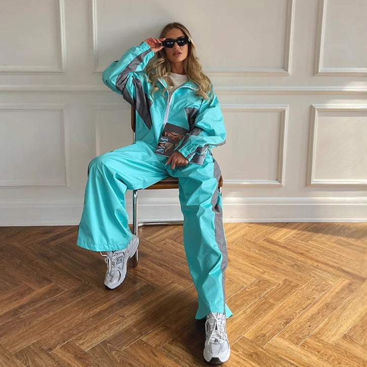 Women's windbreaker tracksuit set in bright aqua and gray, seated view with matching jacket and pants.