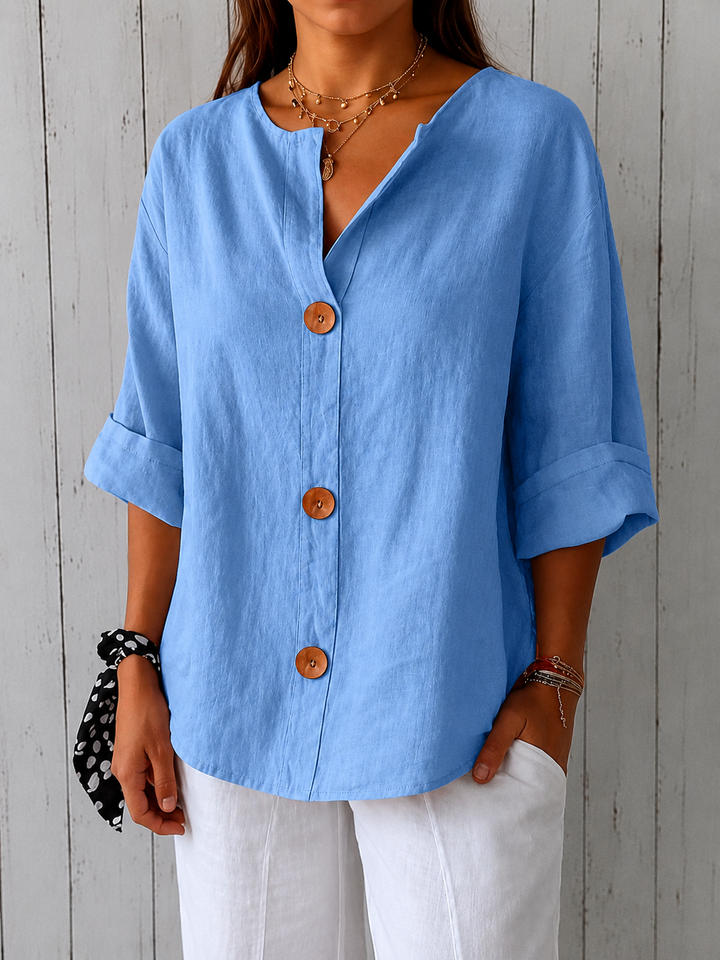 Olivia loose linen blouse in light blue showing the textured linen weave, wooden buttons, stitched cuffs and curved hem.