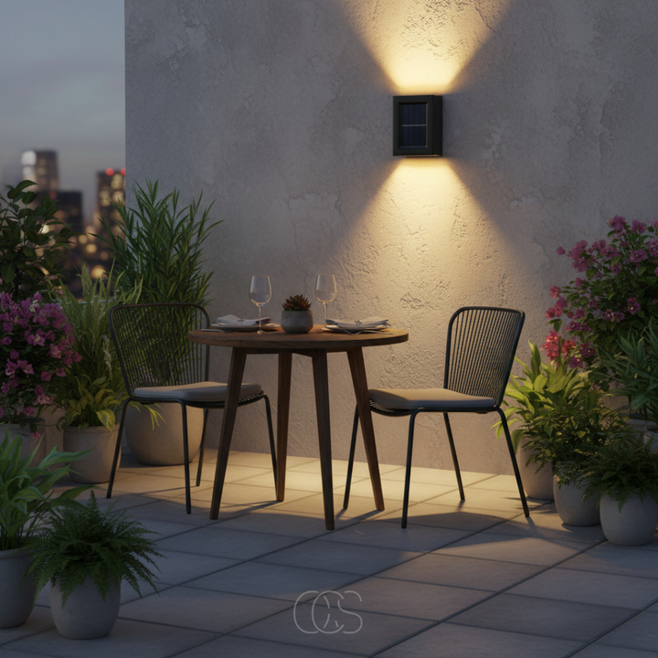 Small black solar wall light casting warm light up and down a textured wall above a bistro table on a dusk terrace. 1