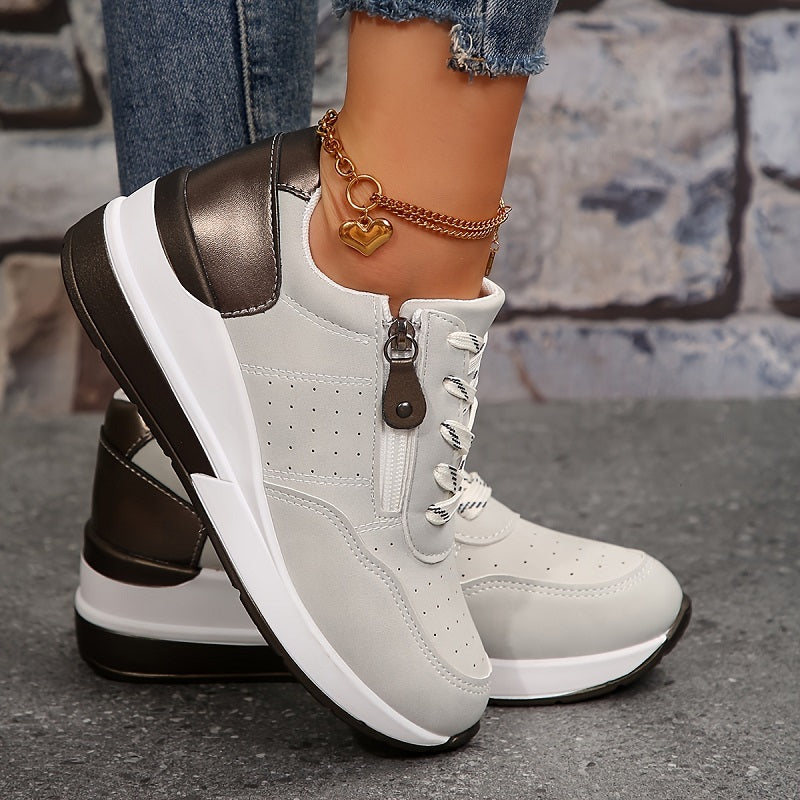 Side view of a light gray wedge sneaker showing the zipper pull, perforated panel, metallic heel tab and thick white sole