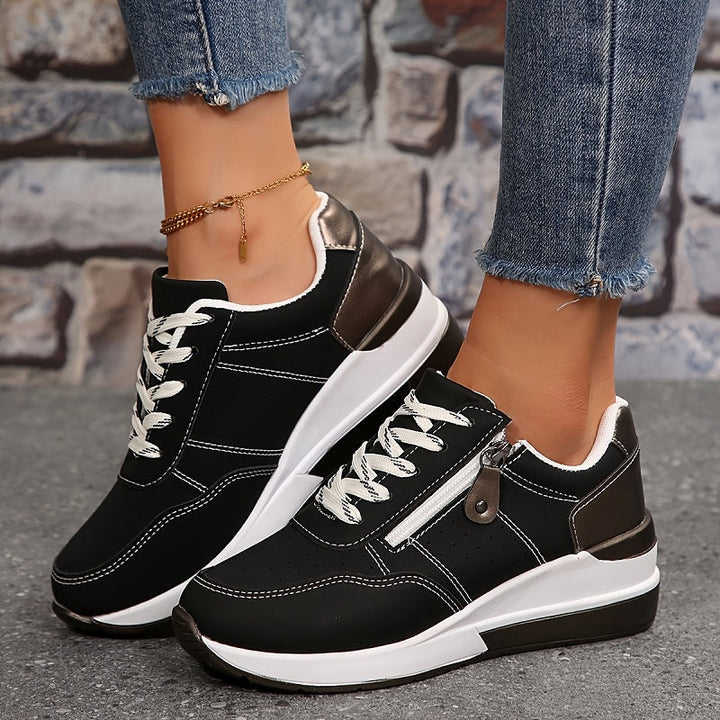 Front three-quarter view of black wedge sneakers with white laces, contrast stitching and side zipper