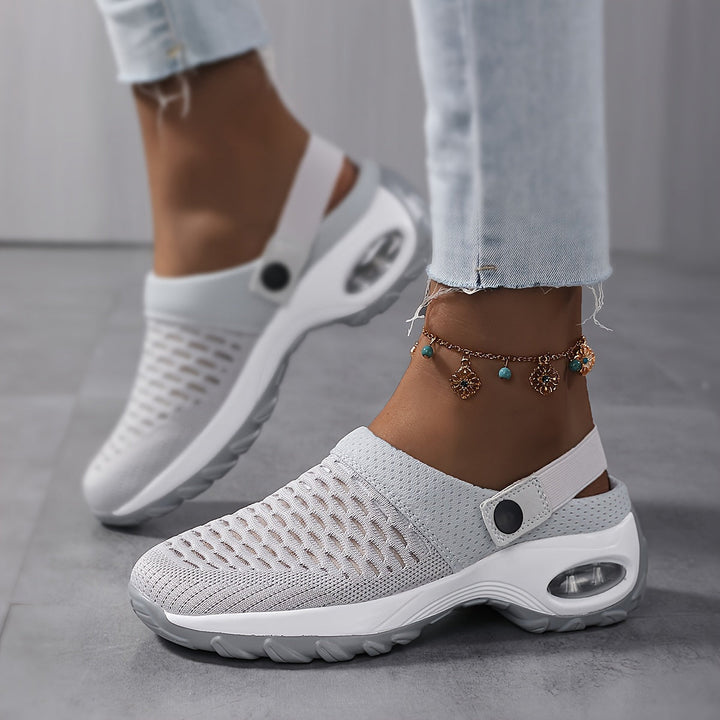 Woman in cuffed jeans and a charm anklet wearing gray mesh clogs, showing the white air-cushion sole and heel strap.